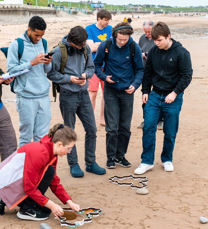 A group of four people stood together in deep thought, while another person kneeling nearby positions a stamper.