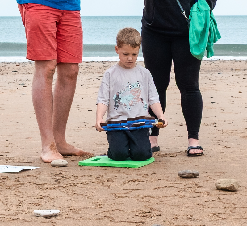 A child kneeling on the sand and holding a stamper, flanked by two adults.