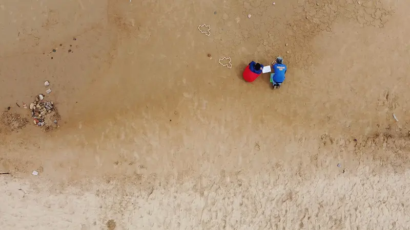 Looking down on two people working on the tiling, coming down from the top towards dryer sand at the bottom.