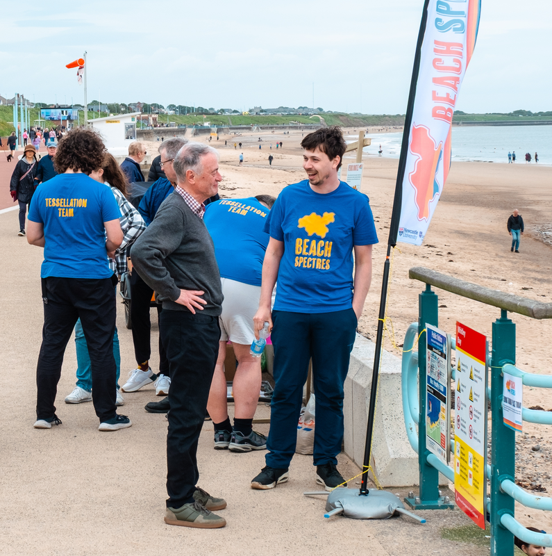 A grey-haired man stood with hands on his hips, listening to a smiling volunteer.