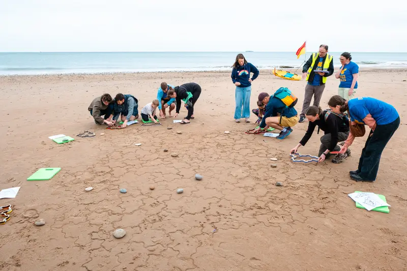 People kneeling around the edge of the tiling, adding more tiles. A volunteer in hi-viz and holding a tablet is pointing at a blank space.