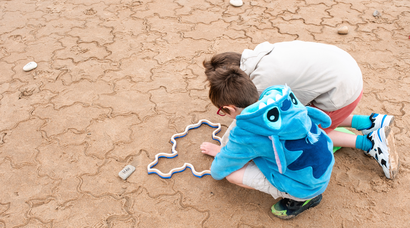 Looking down on two children pressing a stamper into the sand.