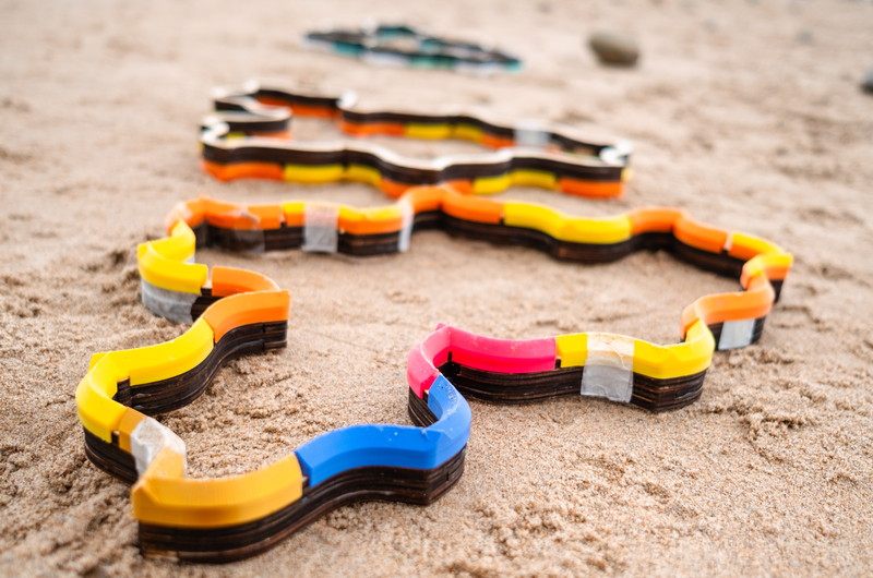 Two Spectre stampers on the sand. The closest one has brightly coloured 3D-printed pieces on the side facing upwards. The one in the background is the other way round.
