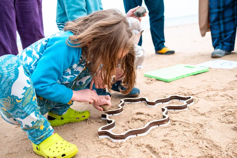 A child squatting and pressing a stamper into the sand.