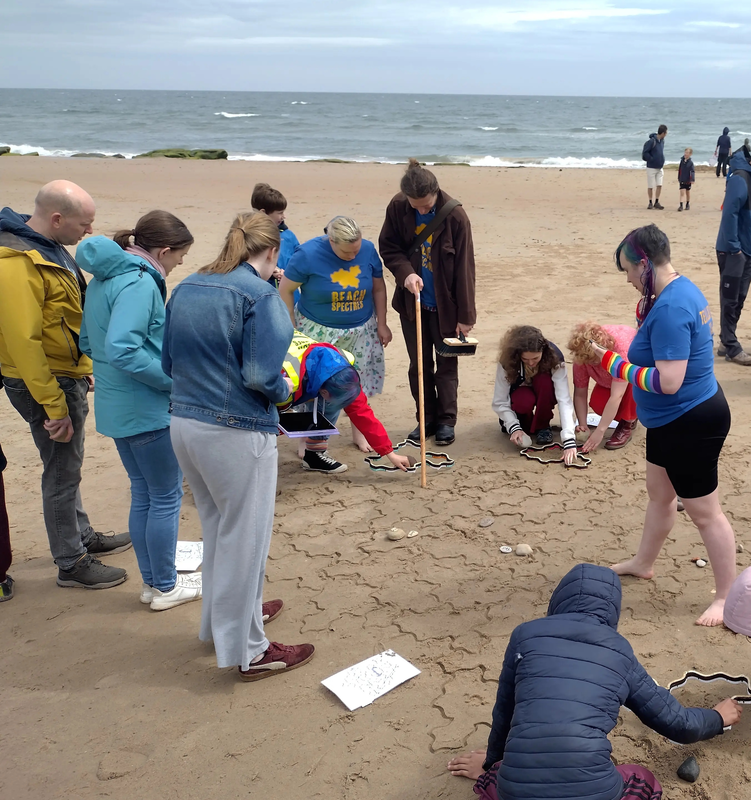 People gathered around an area of tiles, looking at a point a volunteer is pointing to. Another volunteer is standing in the middle of the tiling, awkwardly trying not to disturb the lines.