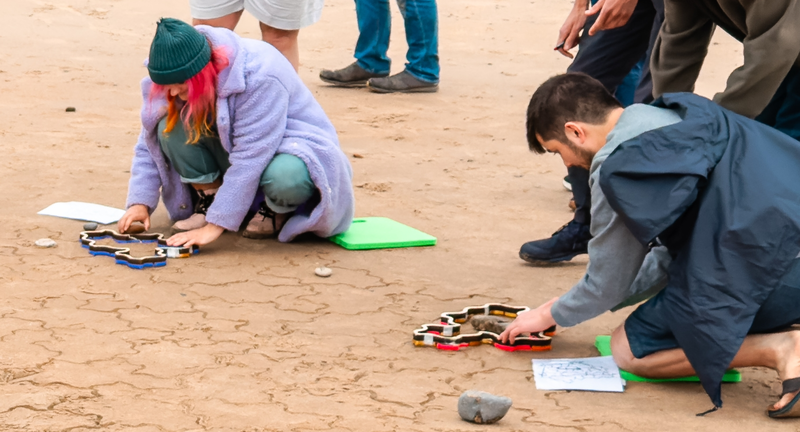Two people kneeling and pressing stampers into the sand.