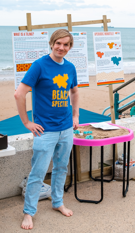 A volunteer dressed in a bright blue Beach Spectres t-shirt, barefoot, stood in front of a tuff tray and a poster board.