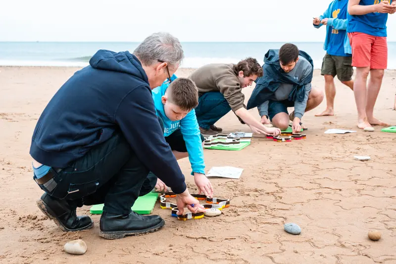 A volunteer holding a stamper still while a child presses it into the sand.