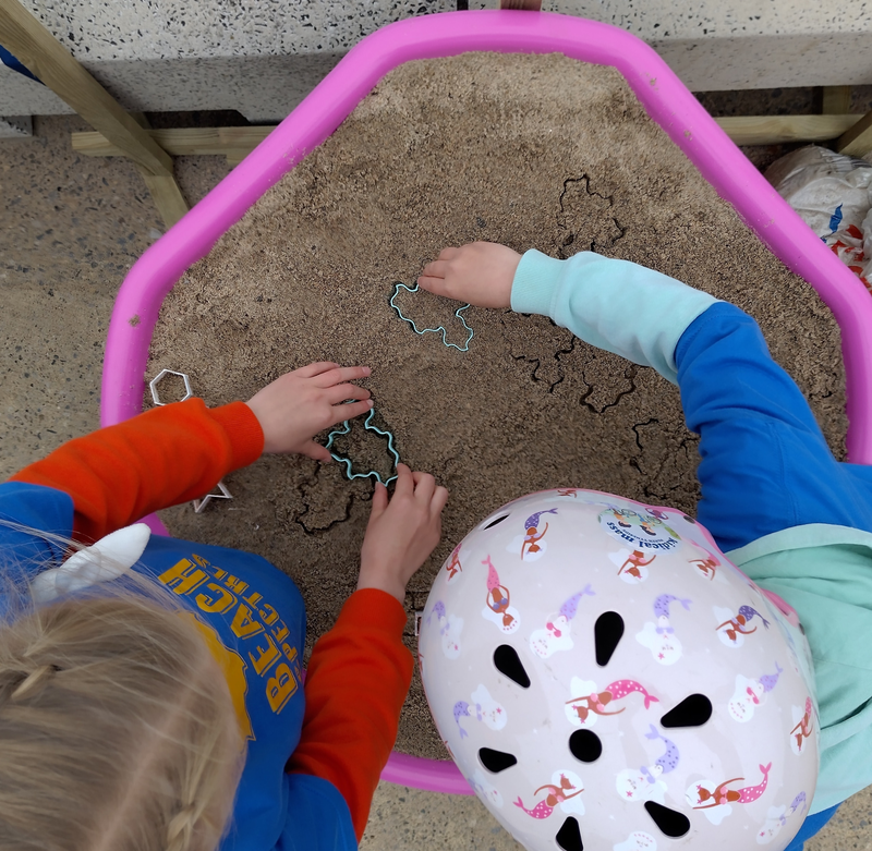 Two children lean over each other to make Spectre tiles in the sand.