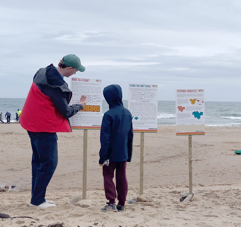 A volunteer pointing at a poster board while a child looks on.