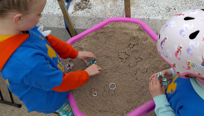 Two children using small stampers to make shapes in the sand.