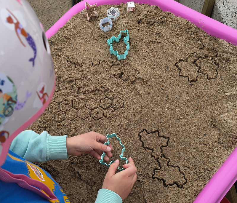 A child uses a small Spectre stamper to make impressions in the tuff tray sand.